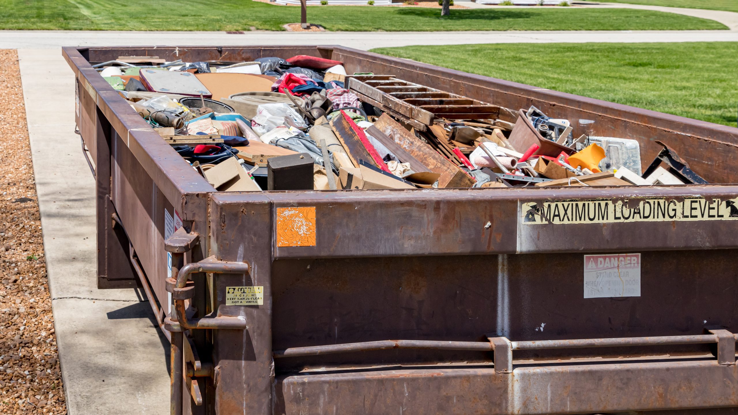 A roll-away dumpster on a residential driveway, loaded with home debris