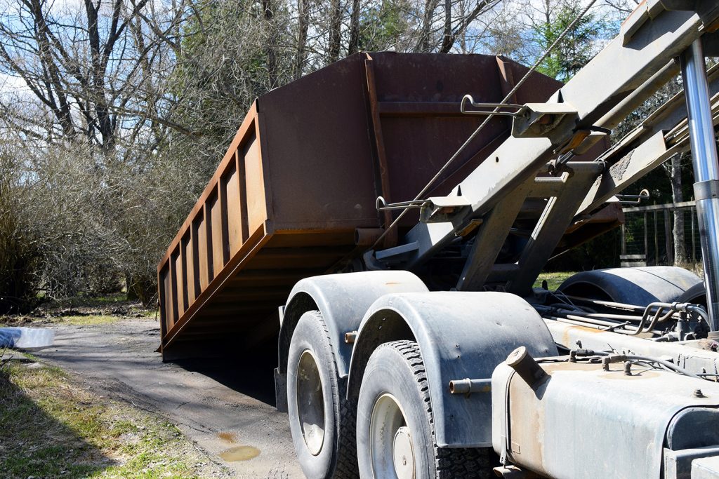 A truck in the middle of dropping off or picking up a roll-off dumpster.