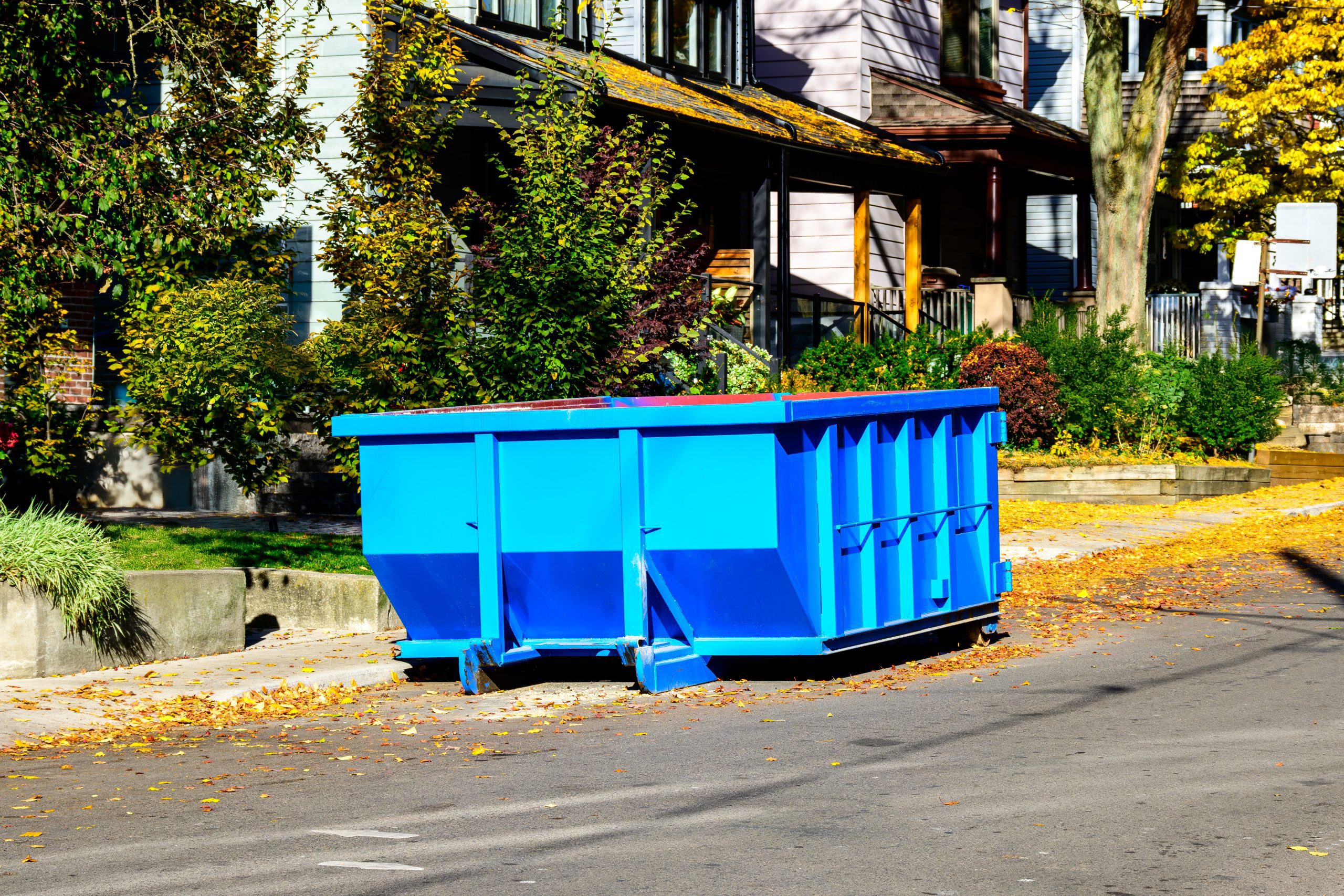 A small blue roofing dumpster rental on the street in front of a suburban home