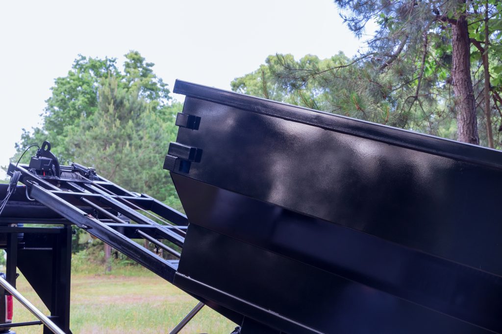 A black roll-off dumpster for roofing being delivered on a lawn