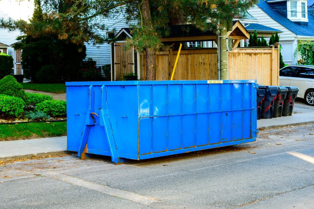 A small blue roll-off dumpster in front of a suburban residential home.