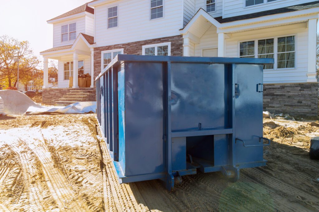 A blue dumpster in front of a house on a lawn.